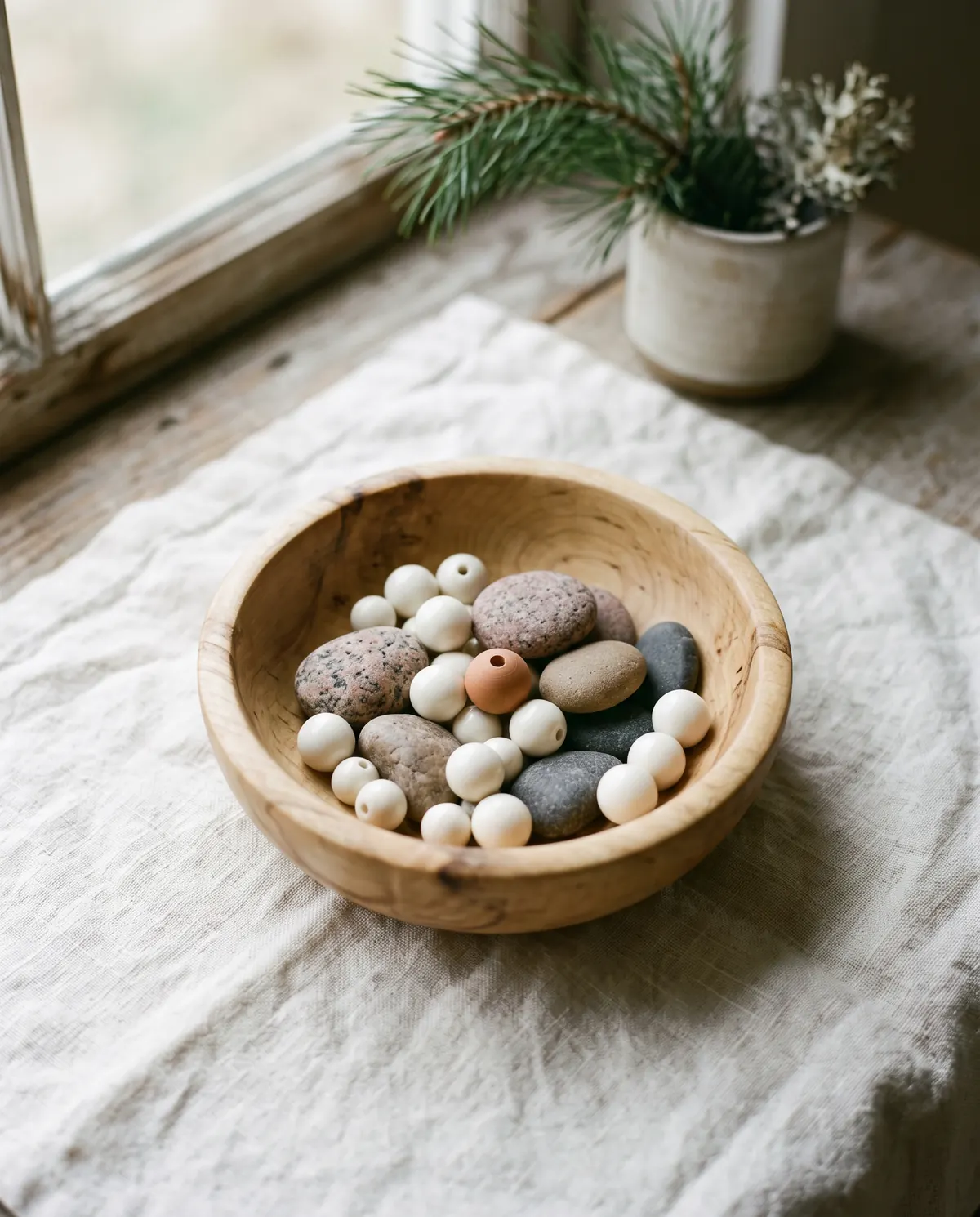 Ivory-white beads and smooth river pebbles in a turned wooden bowl on a linen cloth